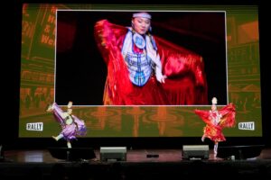 Two women in traditional costumes perform on stage at the Time To rally event.