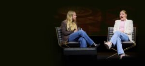 Two women sitting on chairs, engaged in conversation and laughter at the 'Time to Rally' event promoting mindful social media use